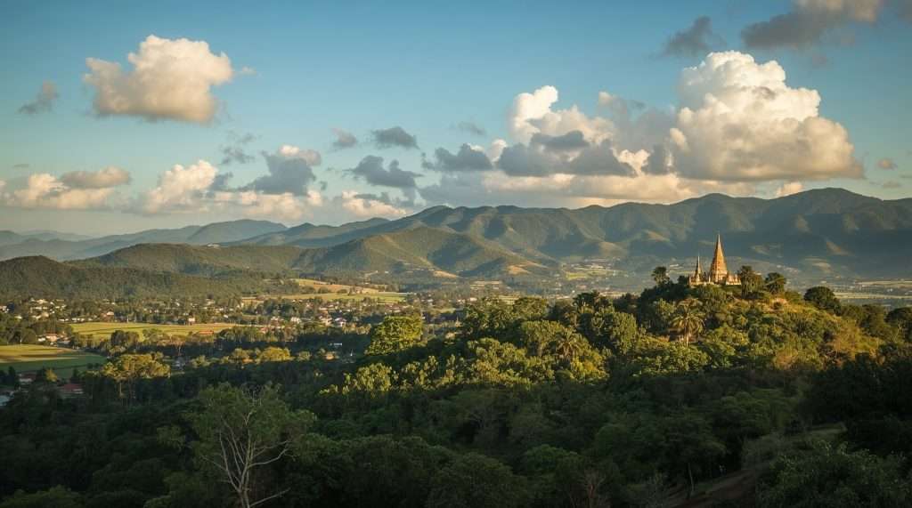 A scenic view of Myanmar's landscape with lush greenery, rolling hills, and a temple structure on a hilltop under a sky with scattered clouds.