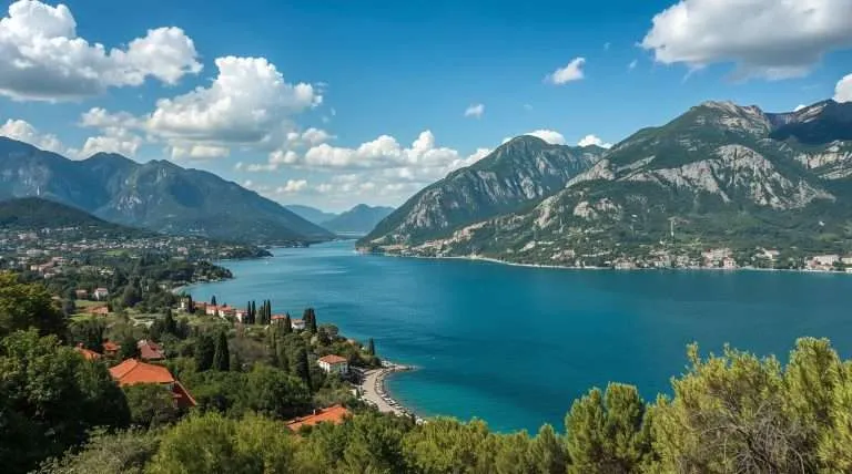 Scenic view of Montenegro with lush green hills surrounding a tranquil blue bay. Red-roofed buildings and tall cypress trees line the coastline under a partly cloudy sky.