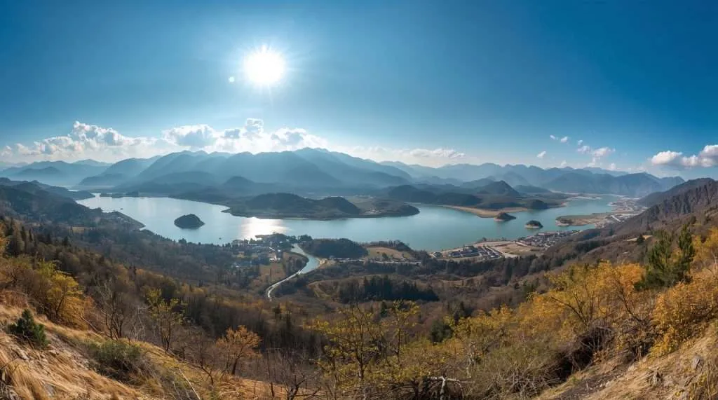 A scenic view of a lush green landscape in China, featuring a winding river surrounded by verdant hills under a blue sky with scattered clouds.