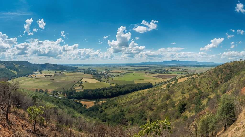 Expansive landscape in Paraguay featuring rolling hills and patchwork fields under a bright blue sky with scattered clouds. Distant mountains frame the horizon.