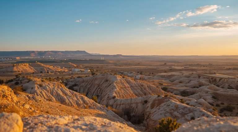 Arid rocky landscape with canyon formations under a partly cloudy sky.