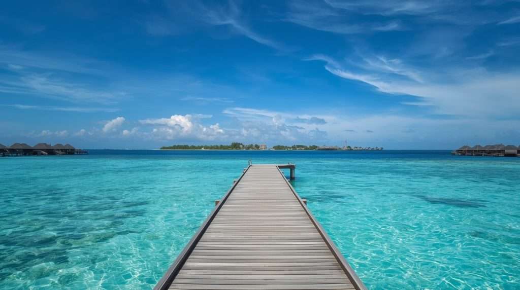 Wooden pier extending over clear blue water under a partly cloudy sky.