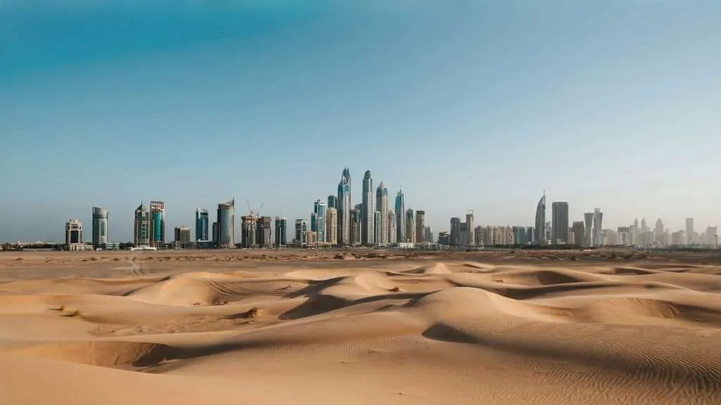 Sand dunes with a distant city skyline in the background.