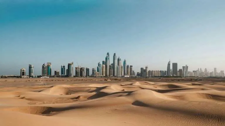 Sand dunes with a distant city skyline in the background.