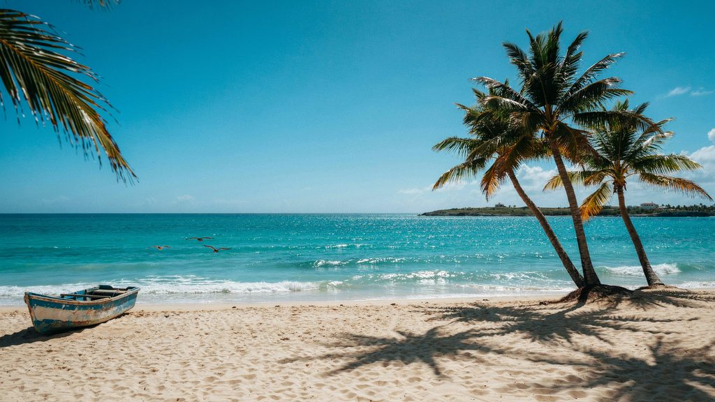 A sandy beach with palm trees, a small boat, and turquoise water in Cuba.