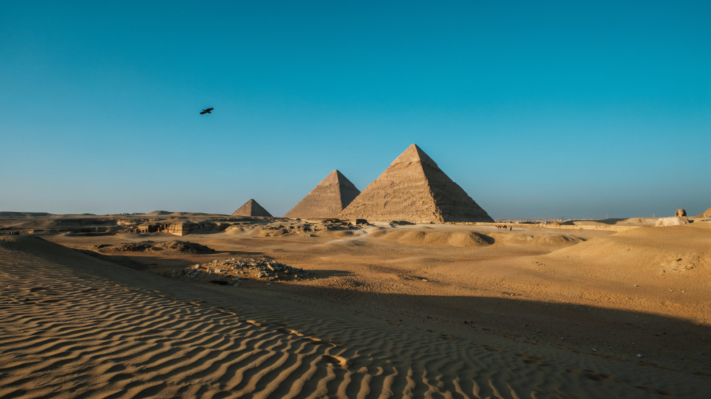 Three pyramids rise from a sandy desert in Egypt.