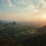 Misty mountains overlook a green valley in Thailand.