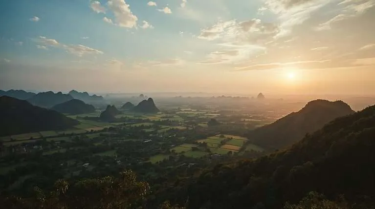 Misty mountains overlook a green valley in Thailand.